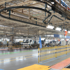 Interior of an automotive assembly plant showing multiple white trucks at various stages of production along a well-lit, organized assembly line. 